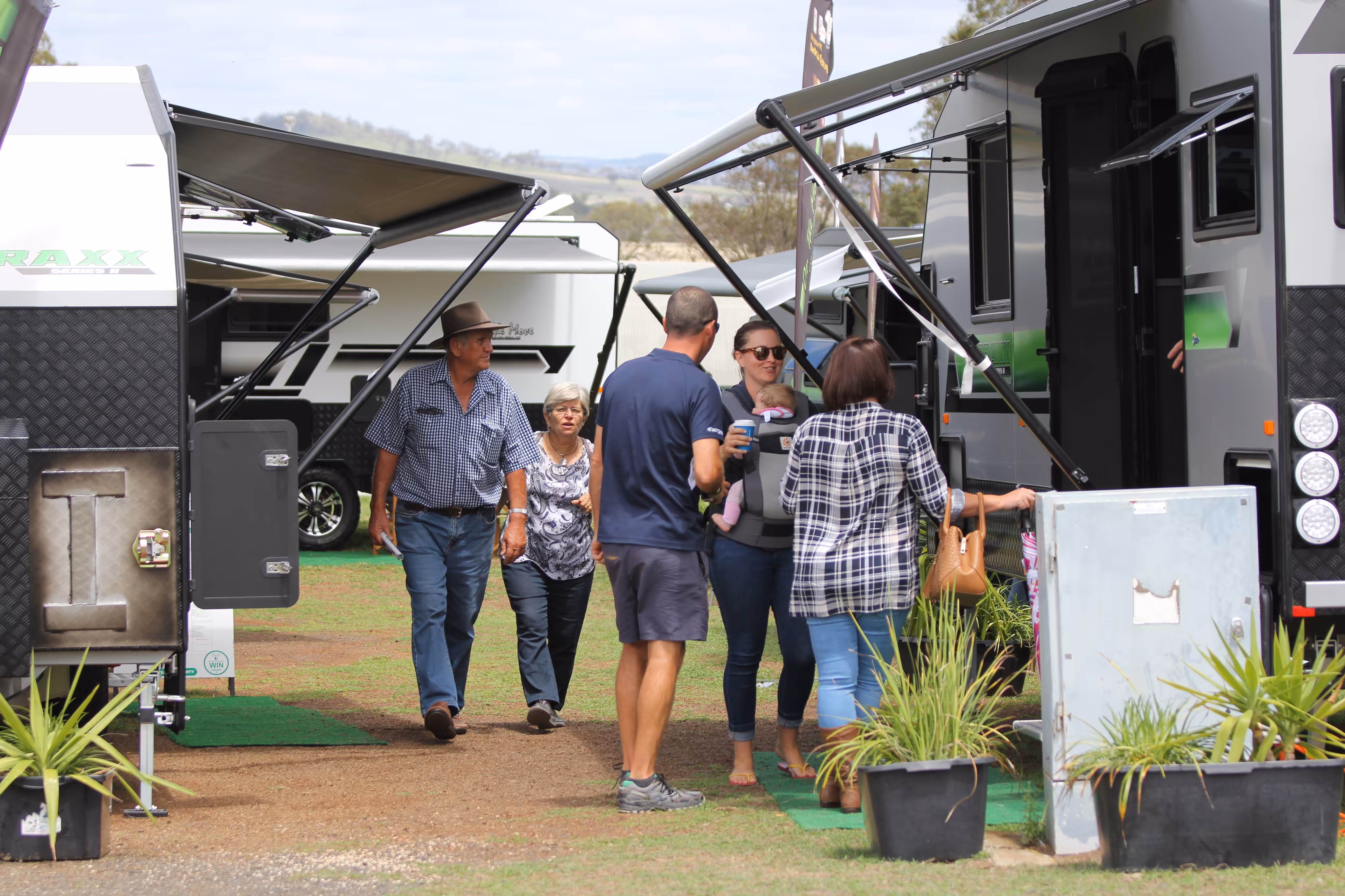 A group of people walk between two caravans at an outdoor expo.