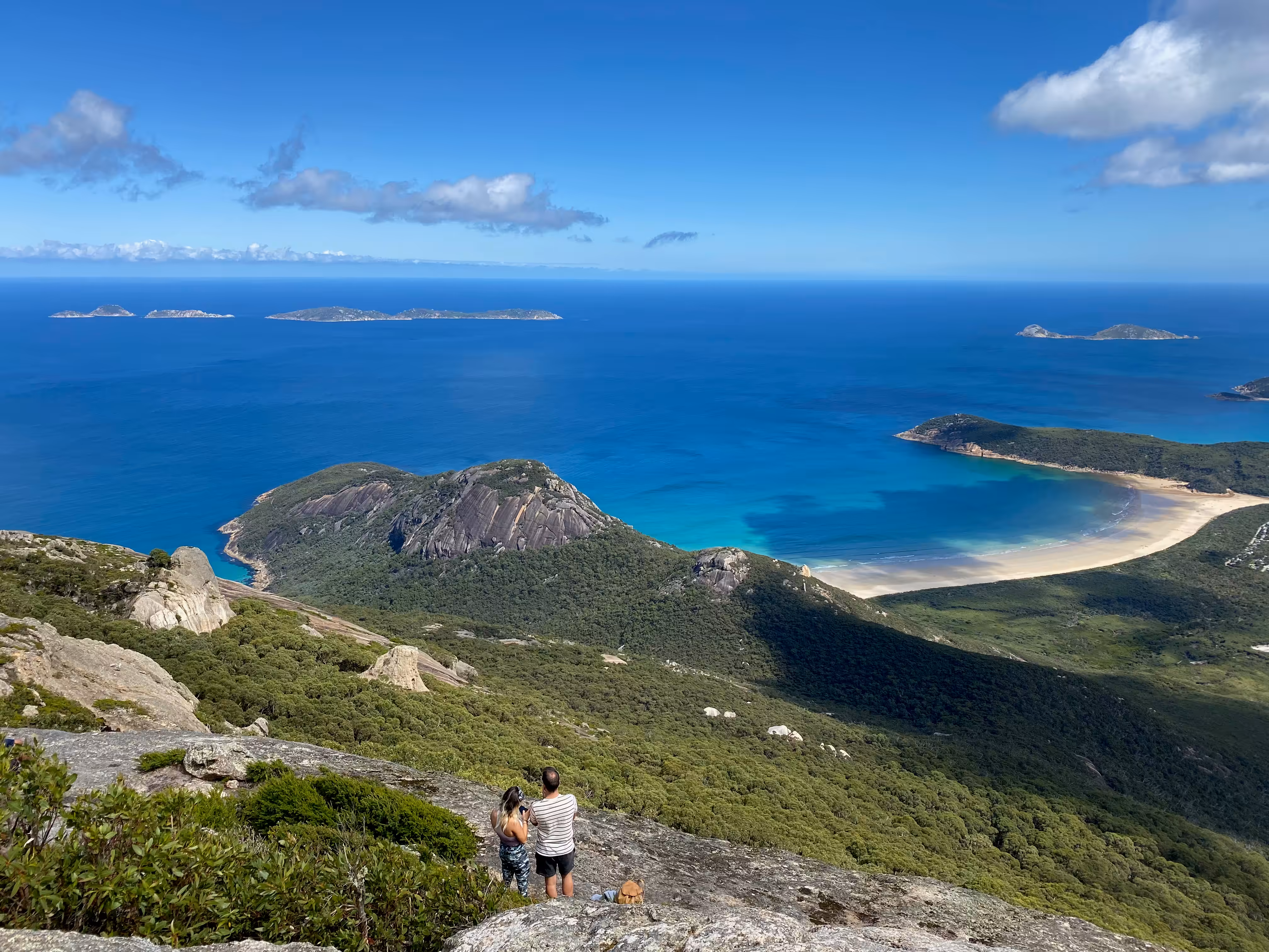 Two hikers stand on a rocky peak looking across the ocean.